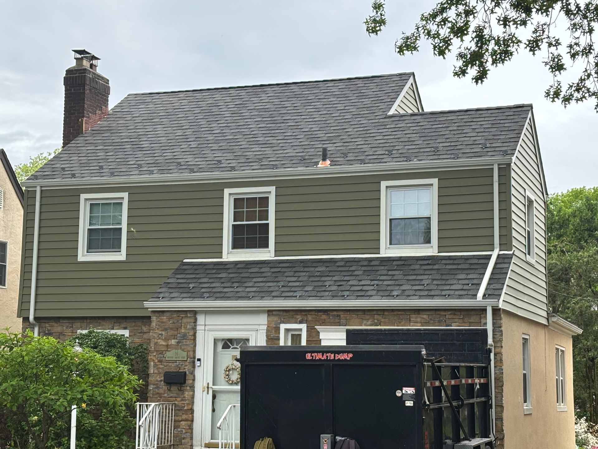 Two-story house with green siding, a gray roof, and a brick base