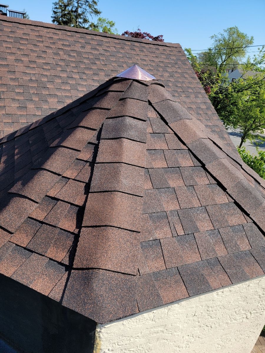 Brown shingled roof with a copper cap, viewed from an upward angle under a clear sky