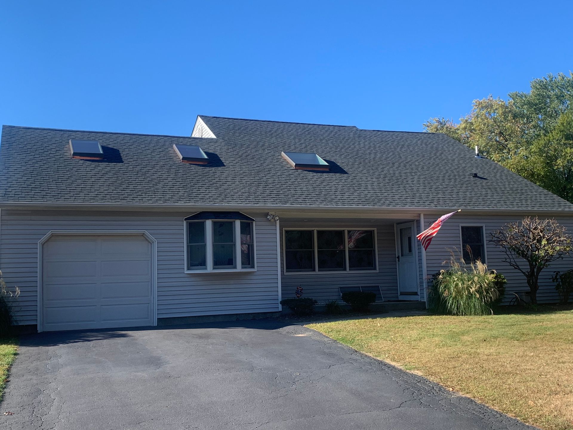 Ranch-style house with gray siding, garage, dark roof with three skylights under a blue sky