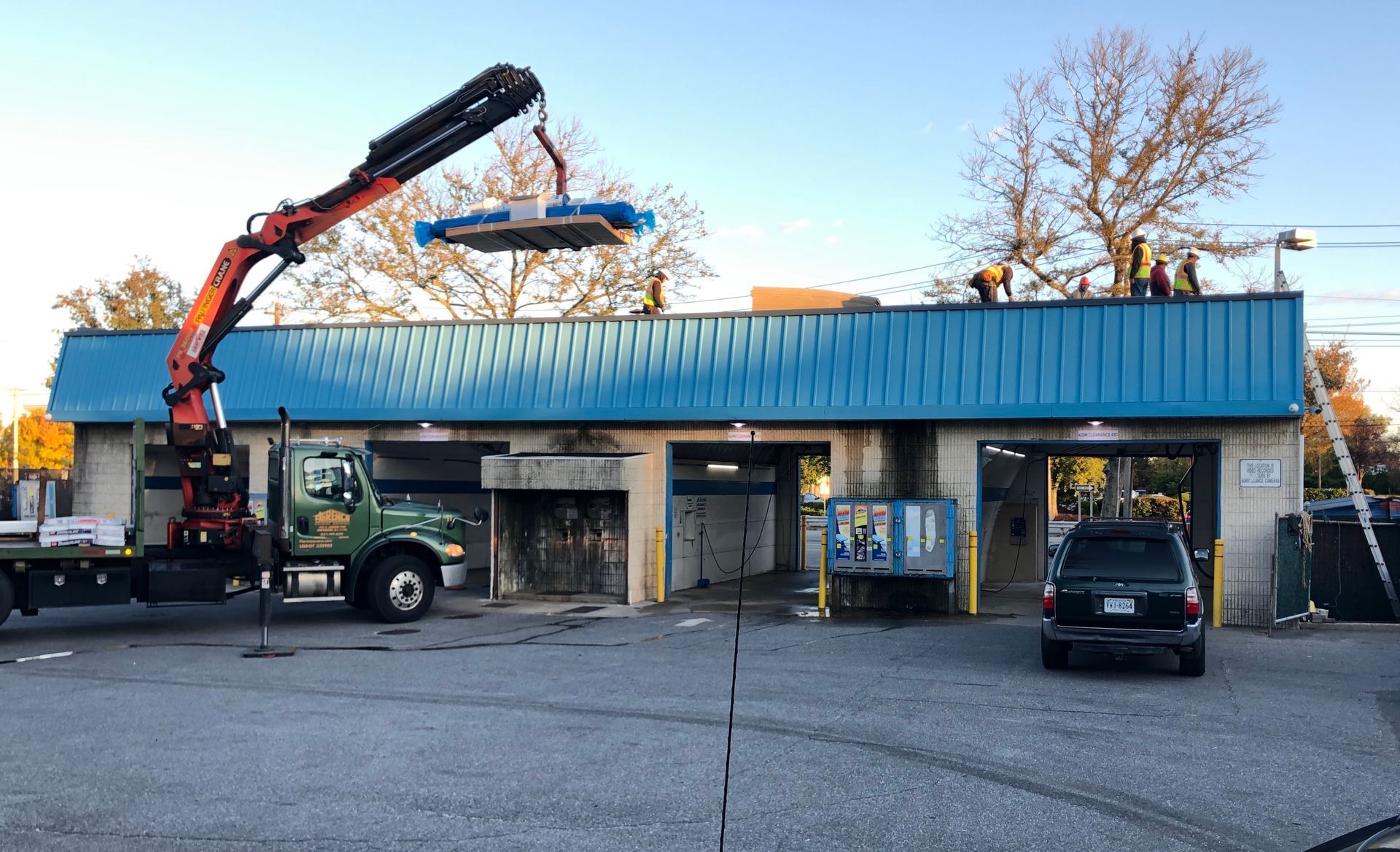 Crane lifting equipment onto a blue-roofed building where workers are present