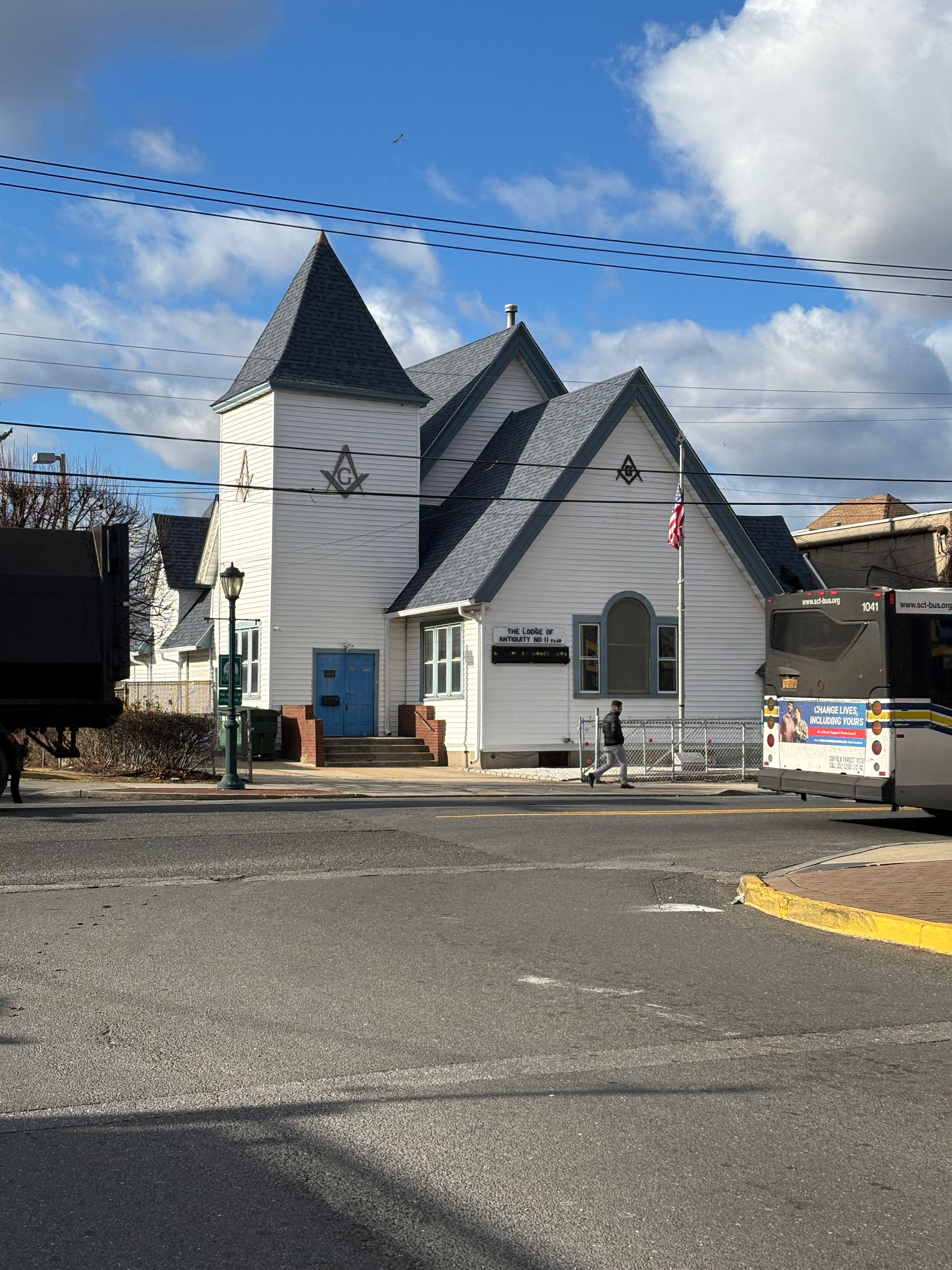 White Masonic lodge building with blue door, gray roof, and flag on pole