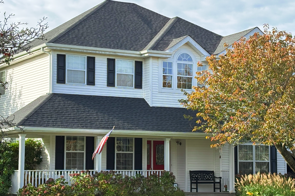 Two-story white suburban house with dark roof, red door, and American flag on the porch