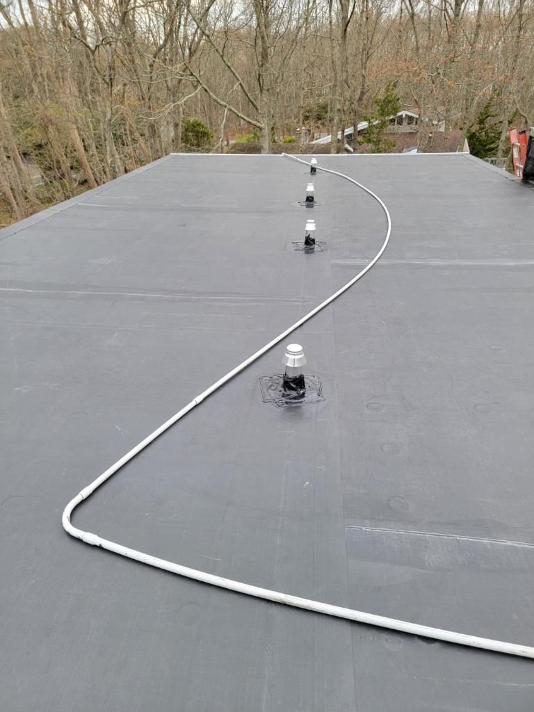 Flat black rooftop with white rope around vertical pipes, trees in the background