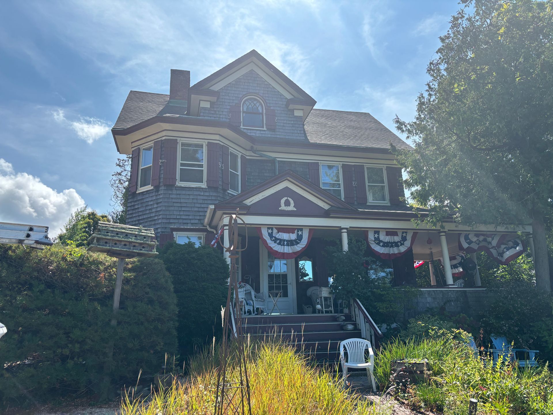 Victorian-style house with red trim, gray siding, and patriotic bunting on the porch