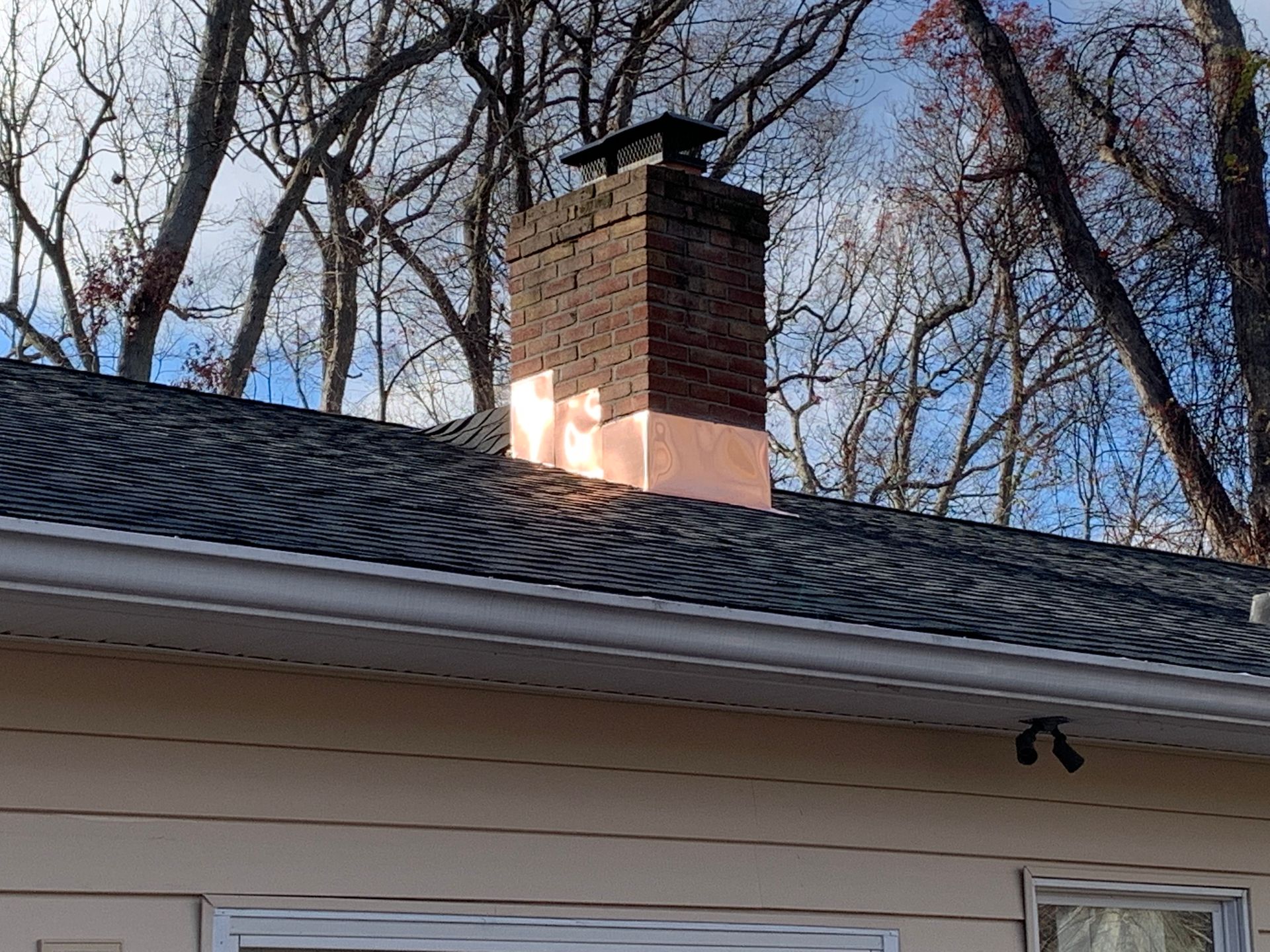 Brick chimney with copper flashing on a roof with dark shingles and light siding
