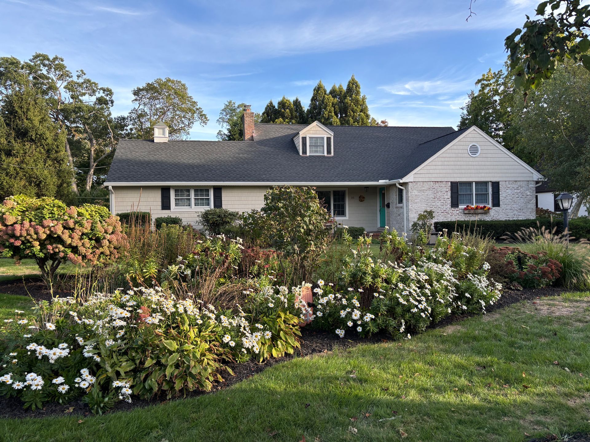 Beige house with a stone facade, flower garden in front, and blue sky