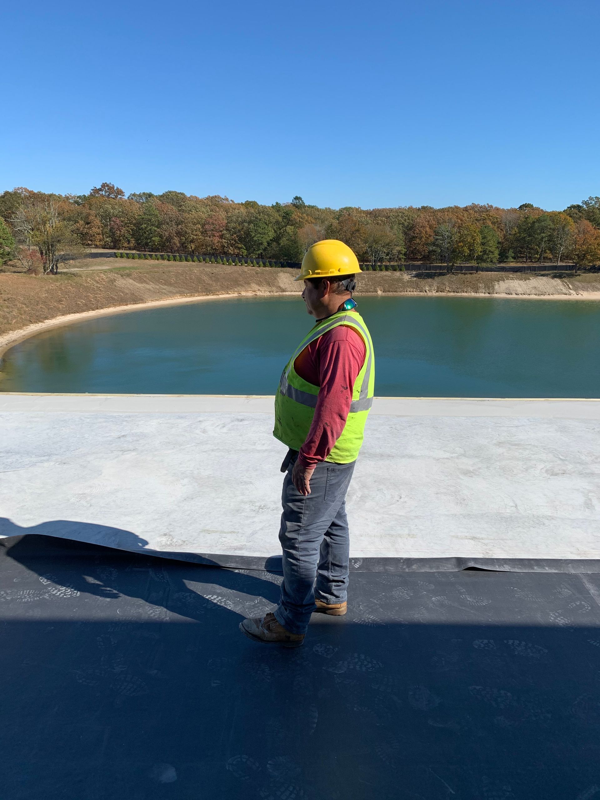 Construction worker in hard hat and vest stands on a roof overlooking a lake