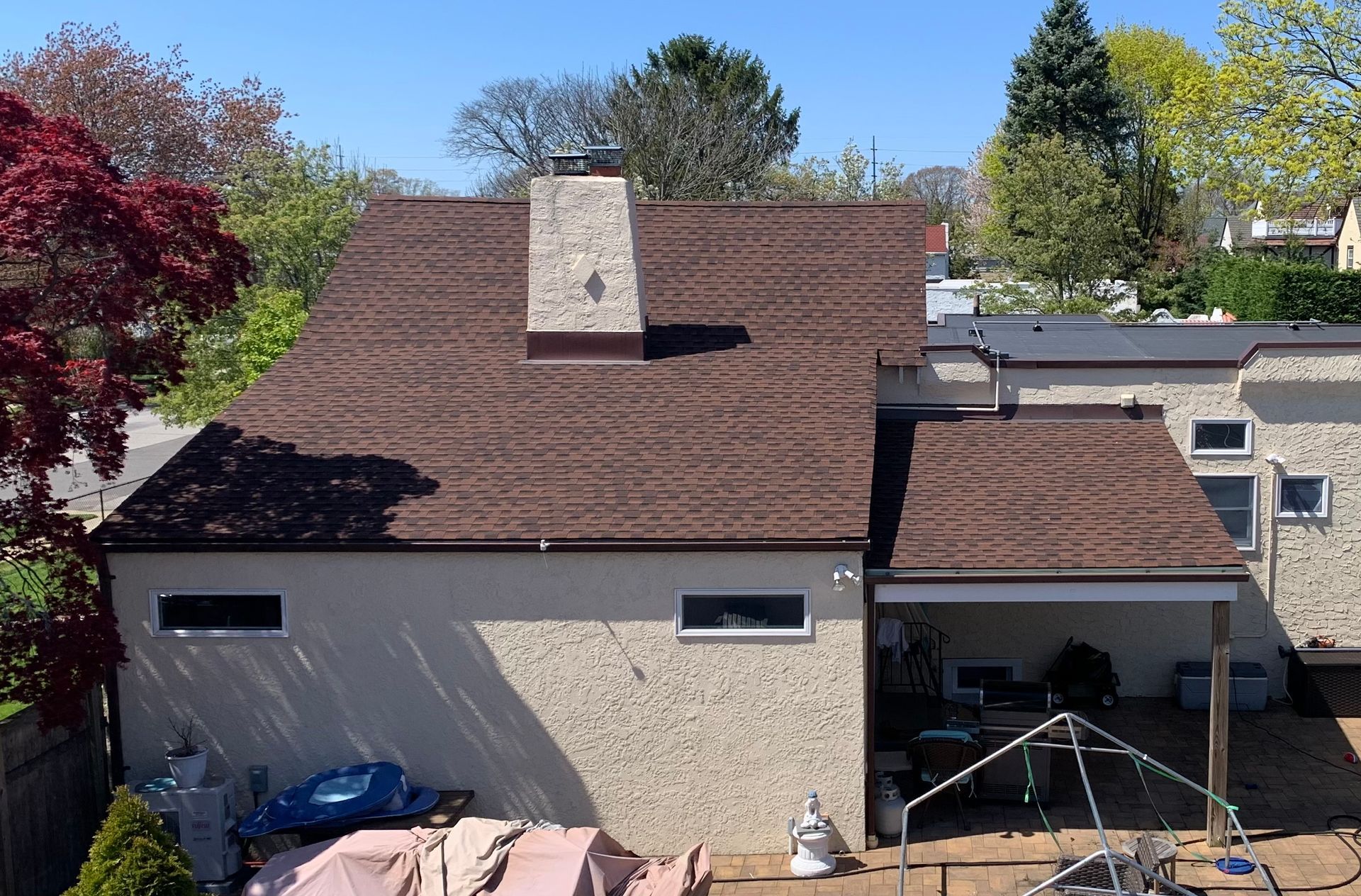 Brown shingled roof on a stucco house with a chimney and patio with outdoor furniture