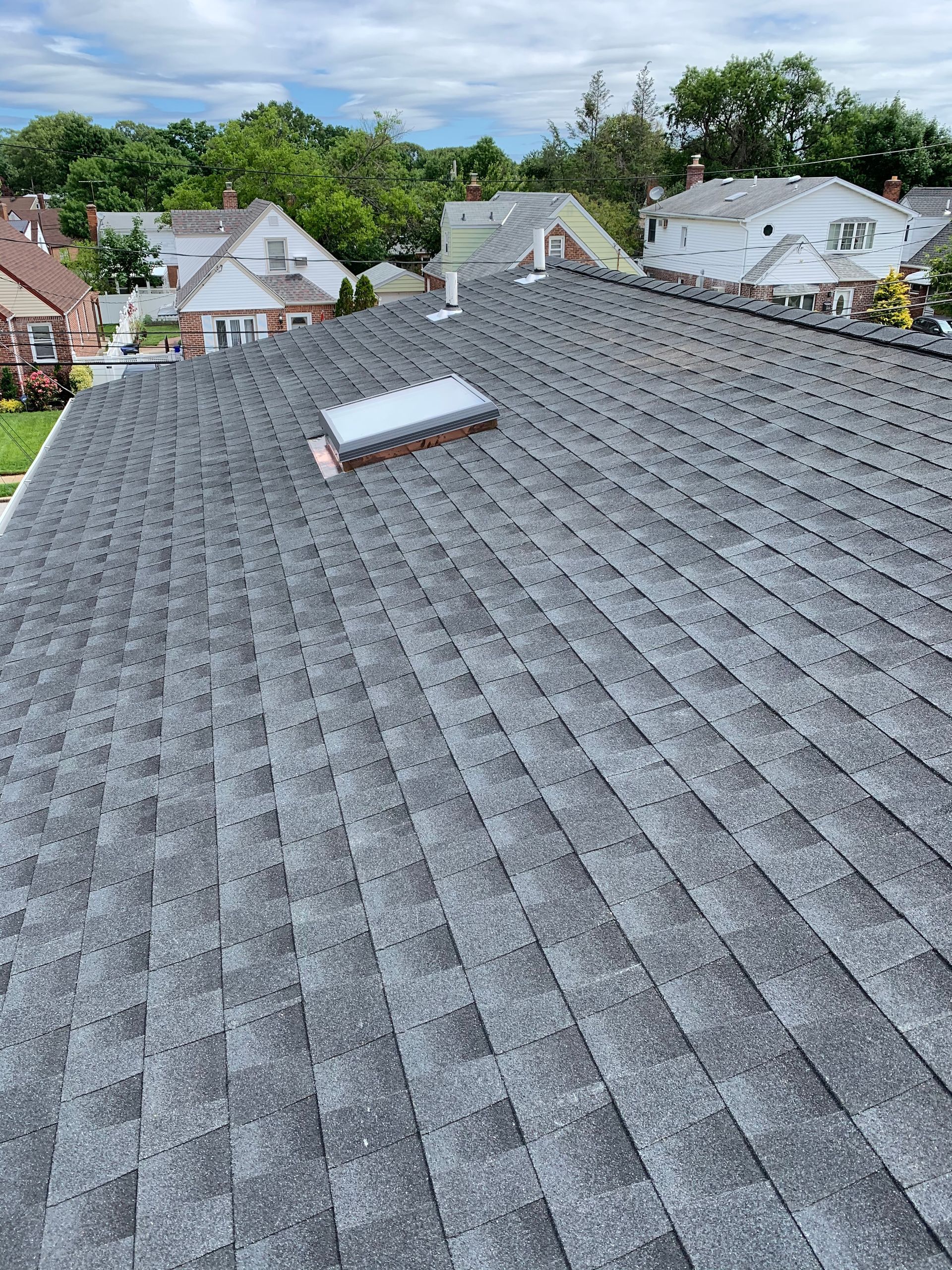 Gray shingle roof with skylight in a suburban neighborhood under an overcast sky