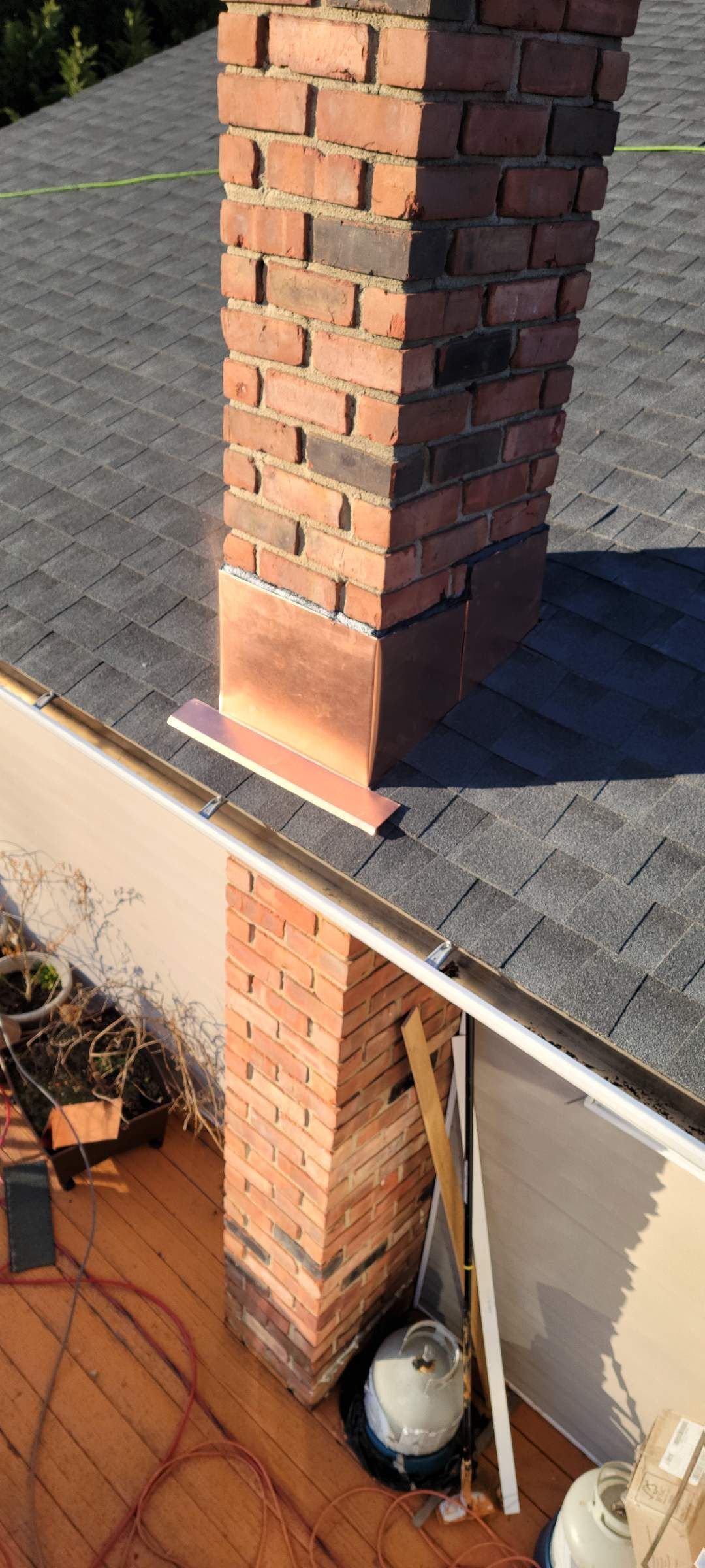 Brick chimney on a dark shingled roof with copper flashing
