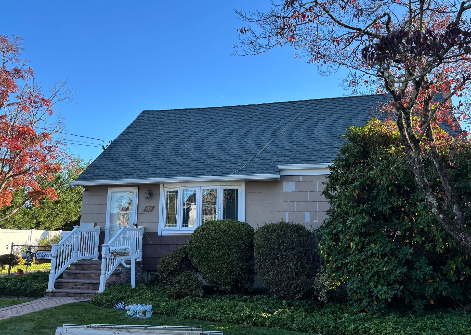Beige house with green roof, white trim, and small front porch with autumn foliage
