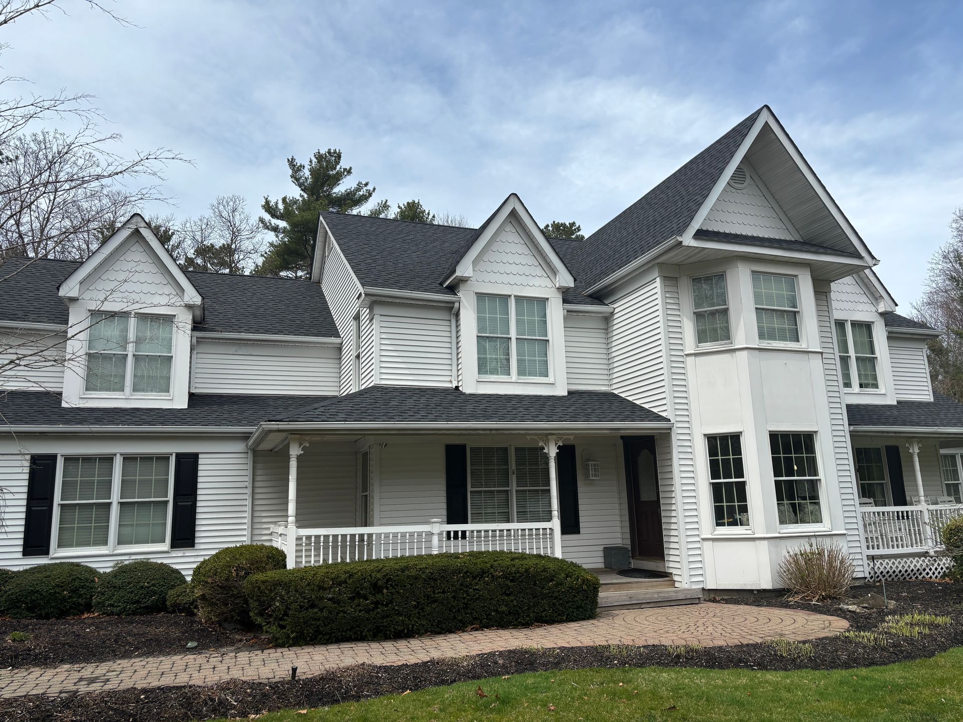White house with black shutters, dark roof, multiple dormers, and a small porch