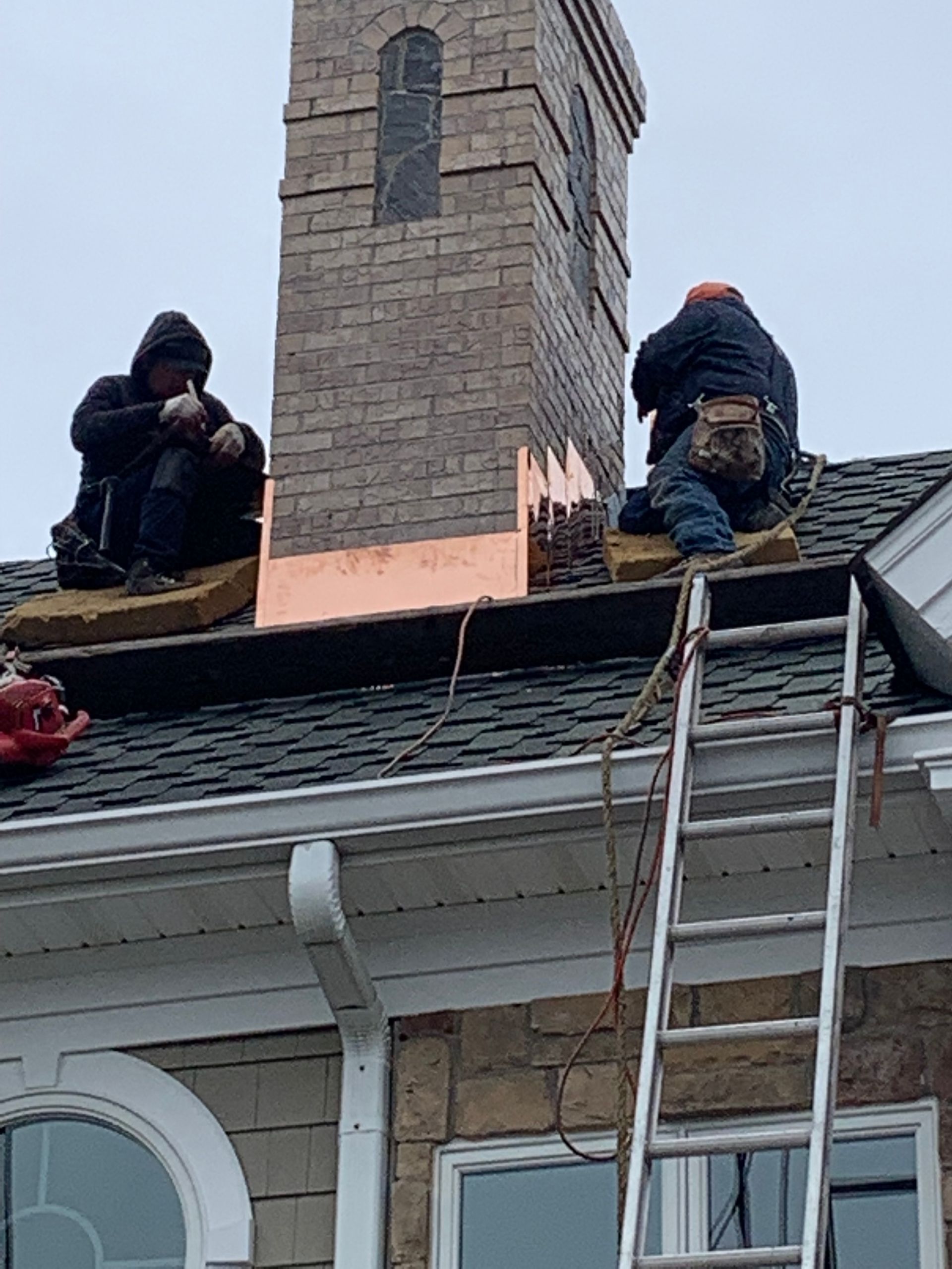Two workers on a roof near a chimney installing copper flashing