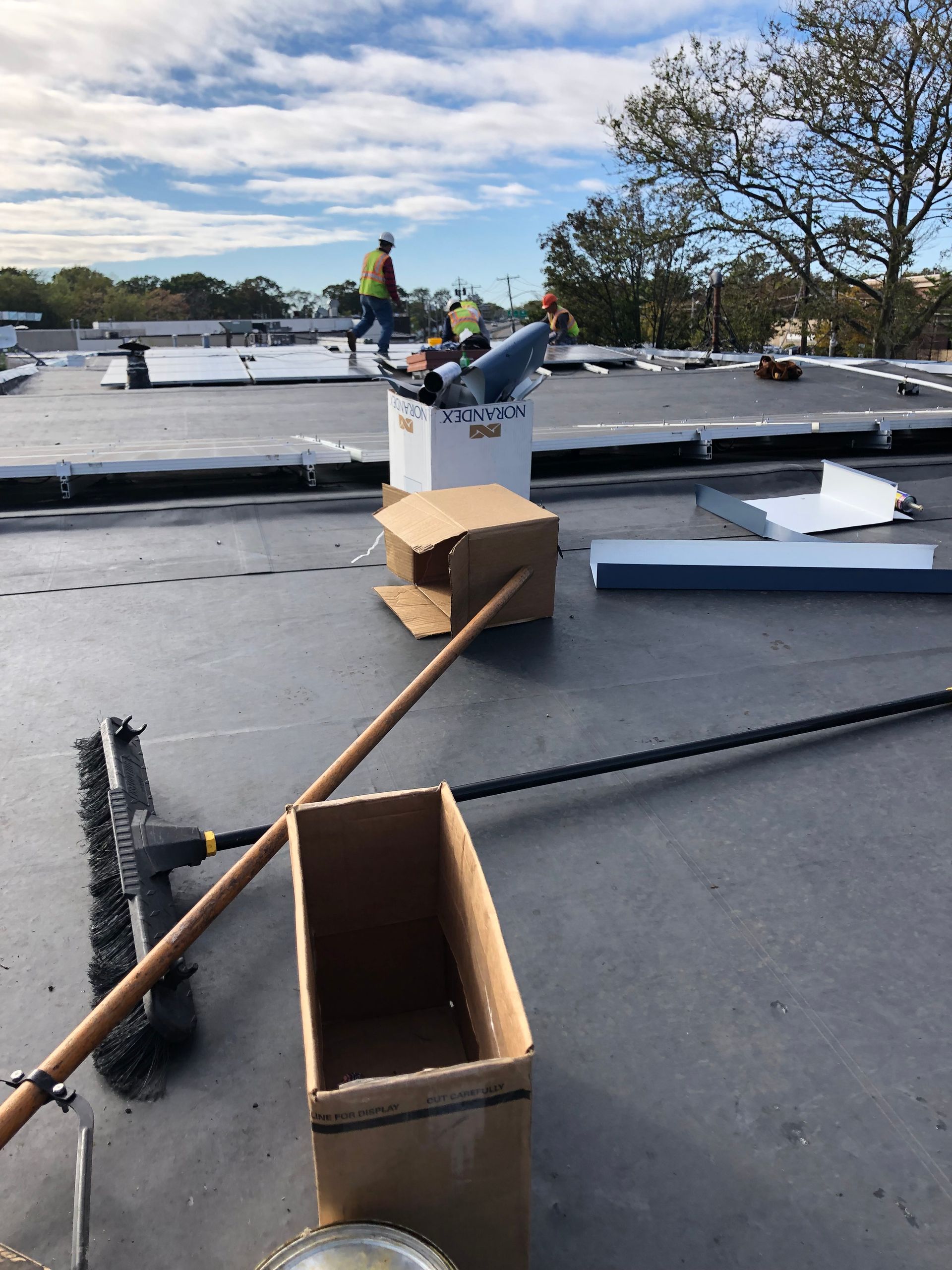 Workers on a flat roof with tools and supplies under a cloudy sky